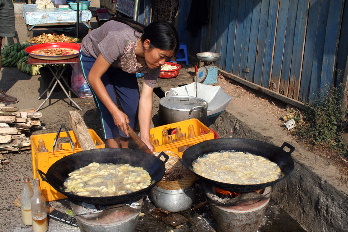 Vrouw bereidt eten op straat in Laos.