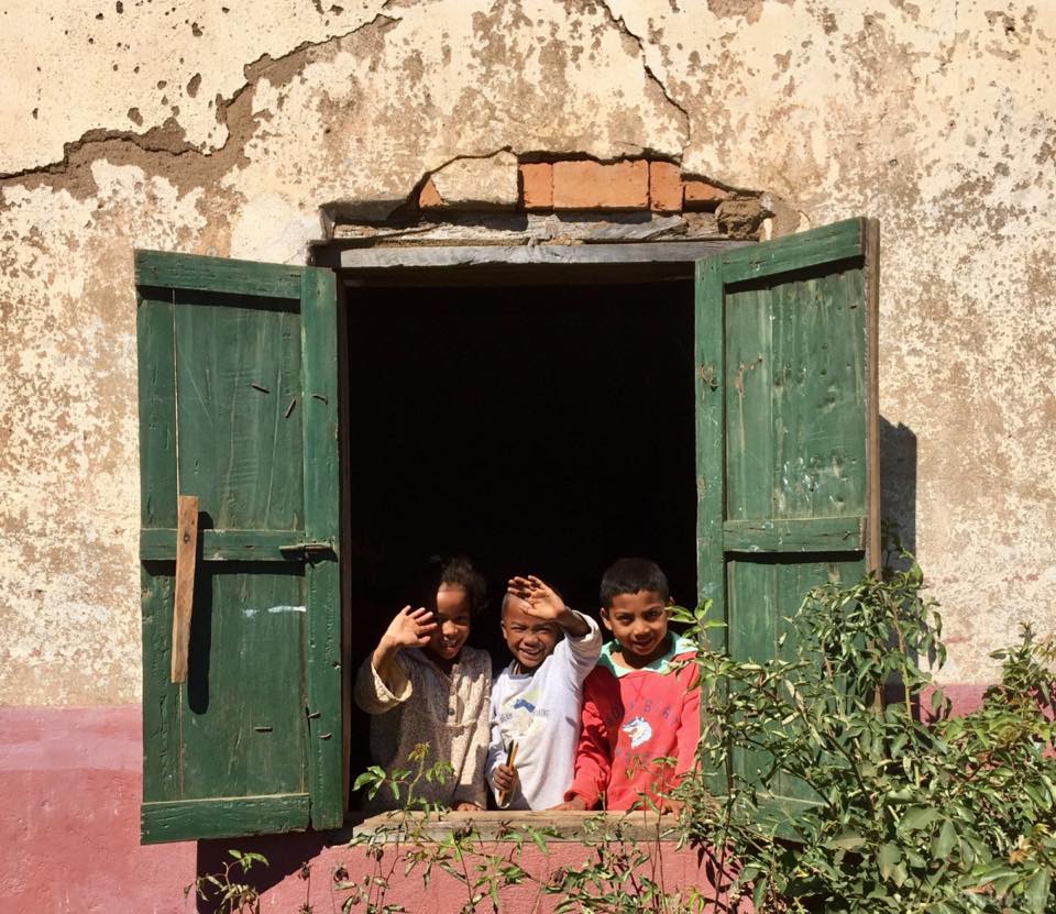 Uit een raam zwaaiende kinderen in centraal Madagaskar