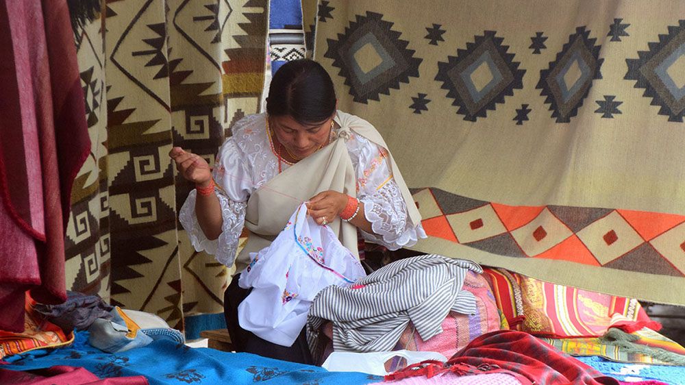 Vrouw borduurt op weekmarkt in Otavalo.