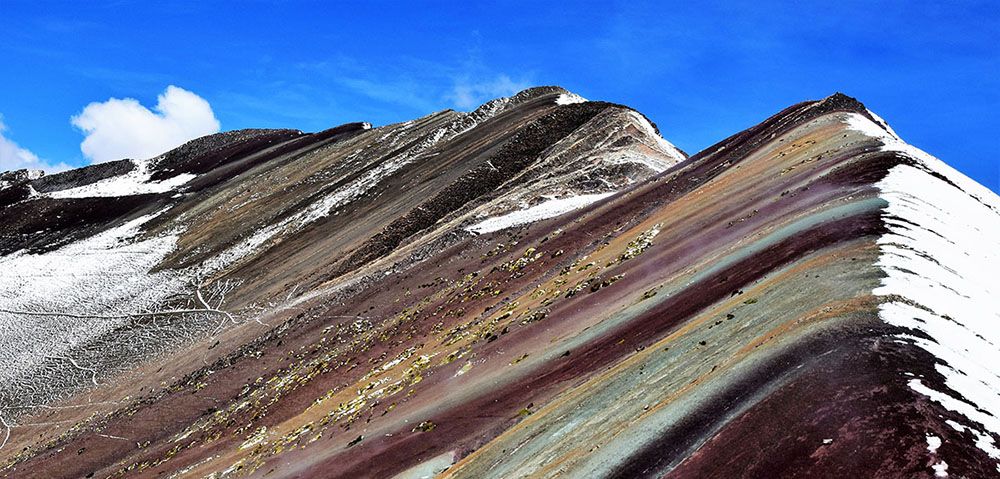 De Rainbow Mountain met aan een kant een besneeuwde helling